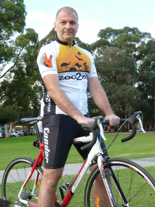 Joe in cycling jersey and lycra, standing astride a bycycle, in the park.