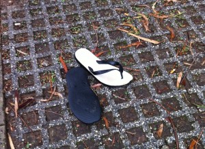 A pair of usable thongs (flip-flops) on the ground, one flipped over exposing the sole.